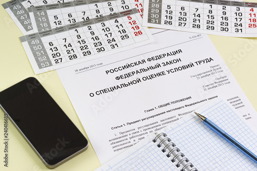 The inscription in Russian "Russian Federation. Federal law on special assessment of working conditions". The study of law. Notebook, pen and smartphone