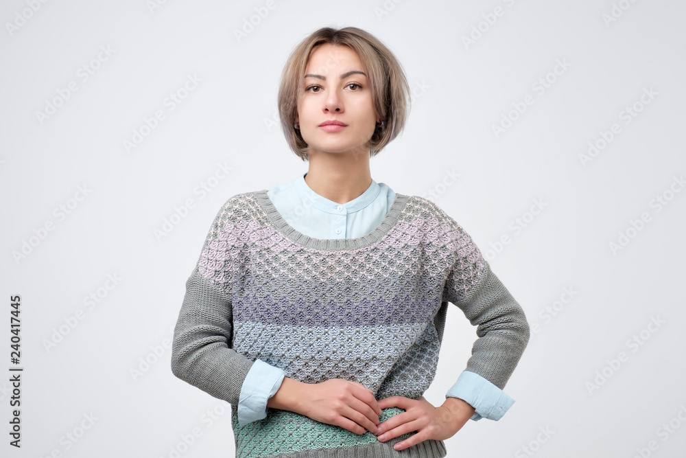 Young woman with short hairstyle wearing sweater standing with neutral expression. Young woman with short hairstyle wearing sweater standing with neutral expression.