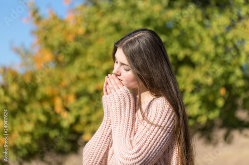 Portrait of pretty young woman in stylish knitted sweater standing on the golden autumn forest on sunny day 