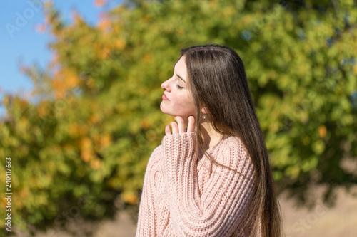 Portrait of pretty young woman in stylish knitted sweater standing on the golden autumn forest on sunny day 