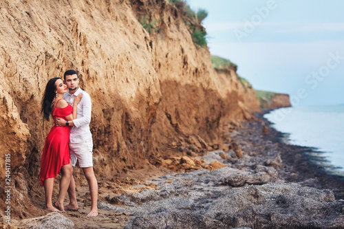 beautiful woman and bearded man hugging near clay rock.