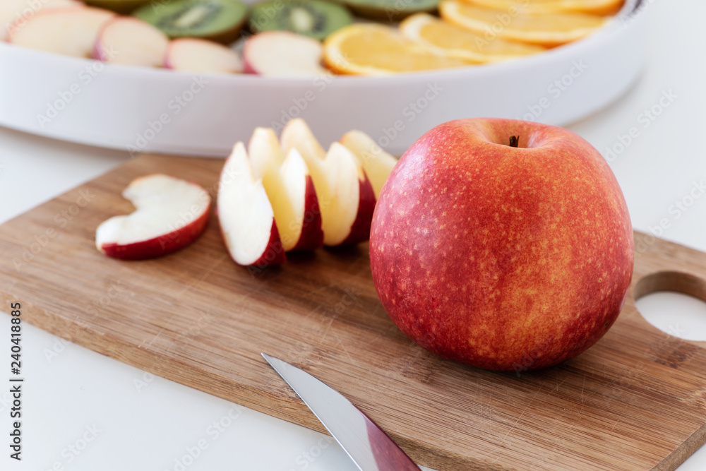 Cutting board with a knife, red apple and slices of apple.