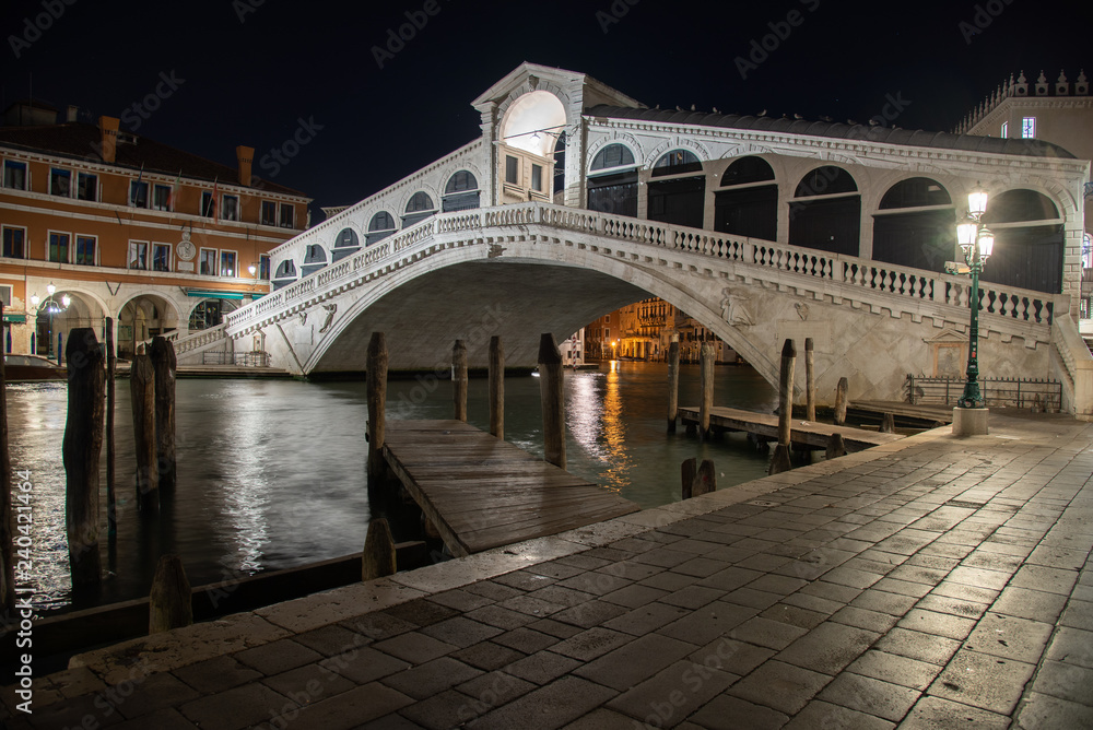 Night photo Rialto Bridge in Venice, Italy. Overview of the bridge illuminated by reflections on the water of the Grand Canal.