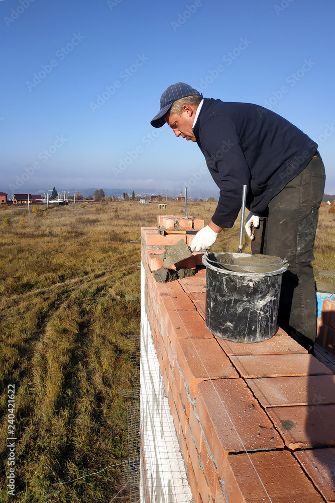 a worker on a building site puts a brick on the sky and that field