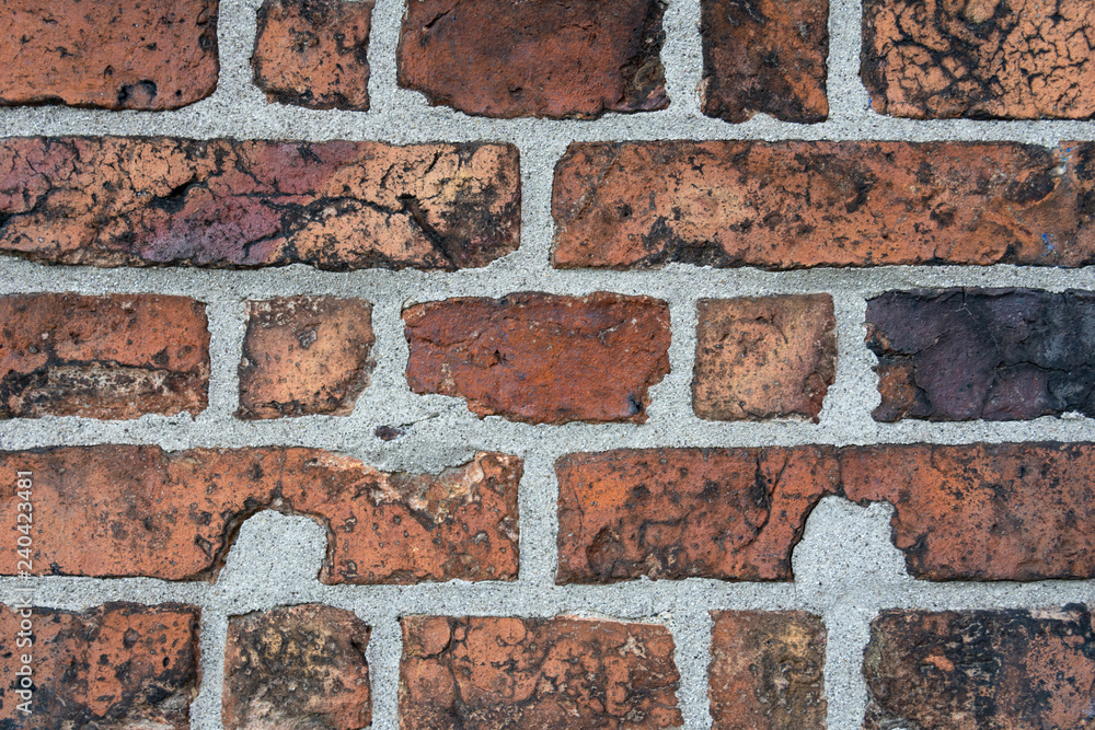 Fototapeta premium Wall of old cracked red brick with black inclusions.