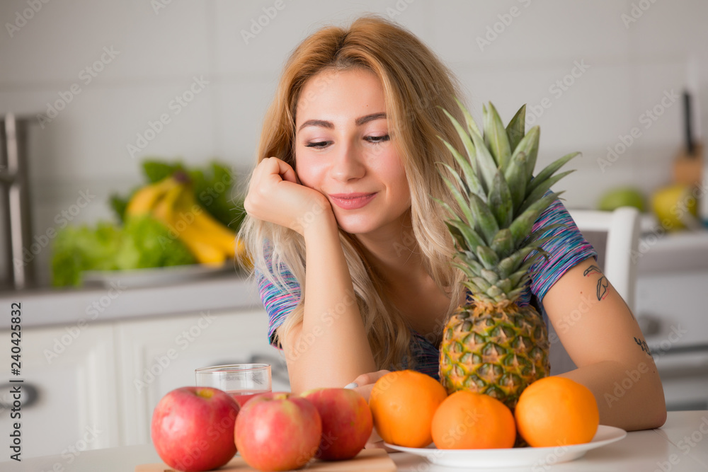 Pretty woman with fruits sitting at the table in kitchen, healthy food Pretty woman with fruits sitting at the table in kitchen, healthy food