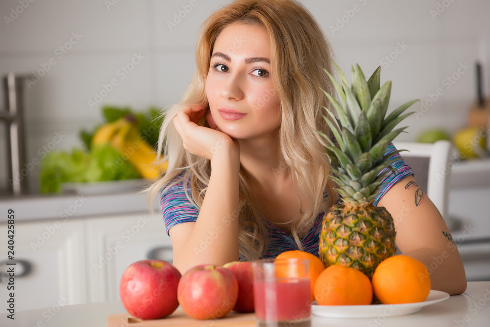 Pretty woman with fruits sitting at the table in kitchen, healthy food