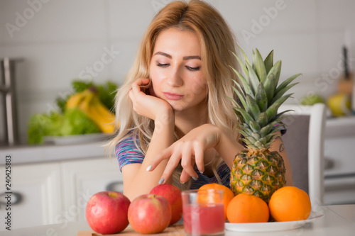 Pretty woman with fruits sitting at the table in kitchen, healthy food