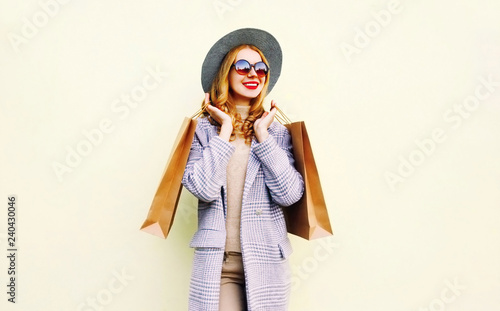 Portrait pretty smiling woman with shopping bags in pink coat, round hat on wall background