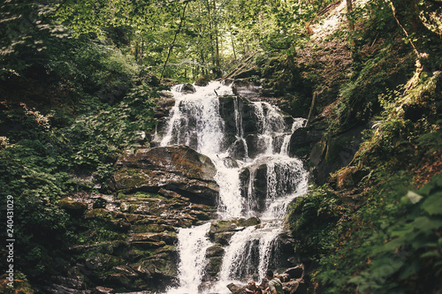 Beautiful waterfall in forest in mountains with cascade with flowing water. Beautiful outdoors scenery. Exploring waterfall in woods. Copy space.