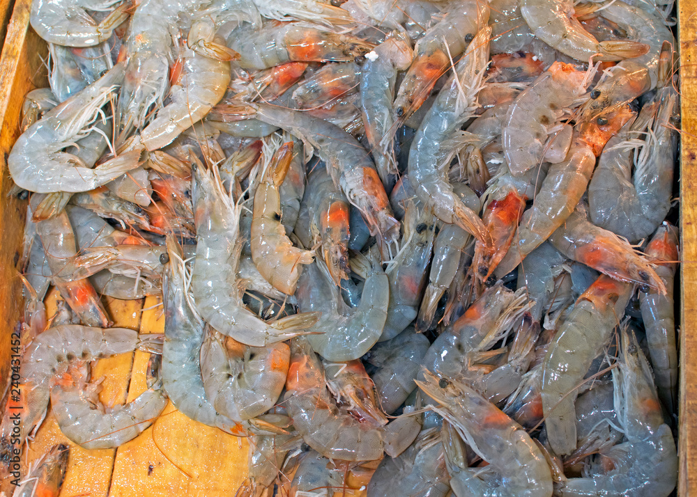 A variety of gray, raw king prawns on a wooden board at a seafood market. Freshly caught shrimps on sale on the counter unpacked