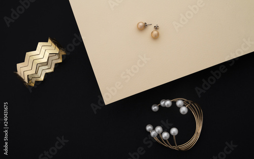 Golden bracelets with pearls and zigzag shape cuff and pair of earrings on black and beige paper background