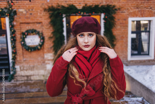 A beautiful girl in a red coat and a beret is walking along the Christmas street.