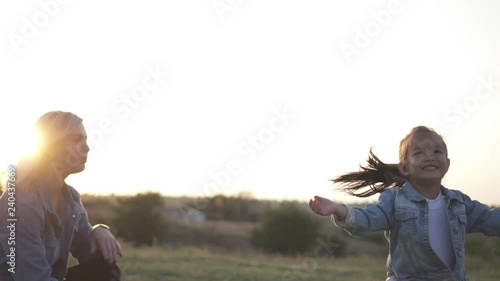 Cute little chinese girl jumping excited and claping her hands. Mixed race family, european mother and asian daughter spending time in the park on sunset. Warm spring or summer season photo