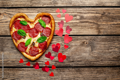 Heart shaped pizza on vintage wooden table background. beautiful red paper saddles Concept of romantic love for Valentine's Day