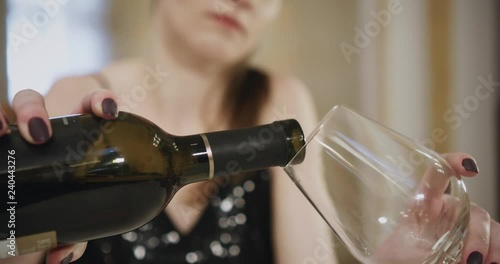 Young woman herself pouring wine in to glass from red wine bottle at the table of the restaurant.