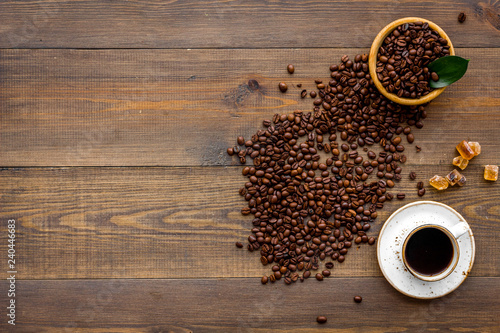Brown roasted coffee beans scattered on wooden background and cup of americano top view mockup
