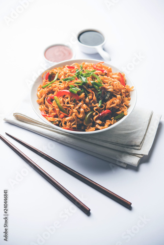 Schezwan veg noodles is a spicy and tasty stir fried flat Hakka noodles with sauce and veggies. served with chopsticks. selective focus photo