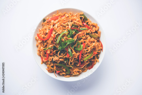 Schezwan veg noodles is a spicy and tasty stir fried flat Hakka noodles with sauce and veggies. served with chopsticks. selective focus photo