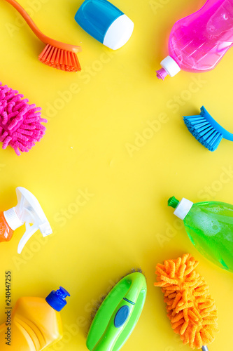 Housecleaning with detergents, soap, cleaners and brush in plastic bottles on yellow background top view mockup