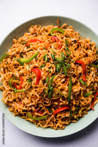 Schezwan veg noodles is a spicy and tasty stir fried flat Hakka noodles with sauce and veggies. served with chopsticks. selective focus