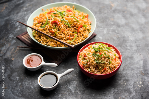 Schezwan veg noodles is a spicy and tasty stir fried flat Hakka noodles with sauce and veggies. served with chopsticks. selective focus photo