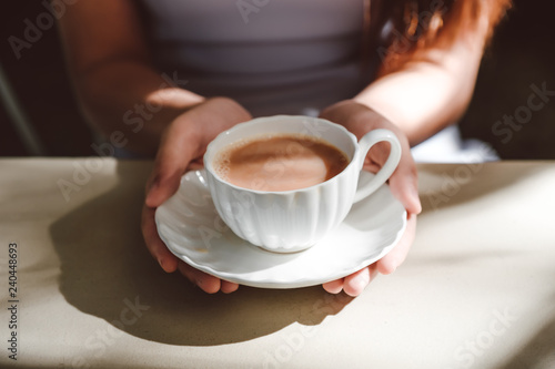 Female in grey dress hands holding a vintage cup of coffee over white table 