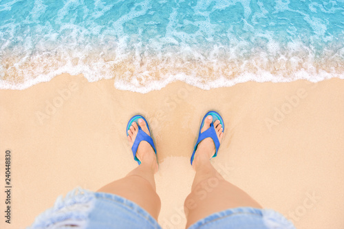 Feet with sandals shoes on sea sandy beach and clear wave