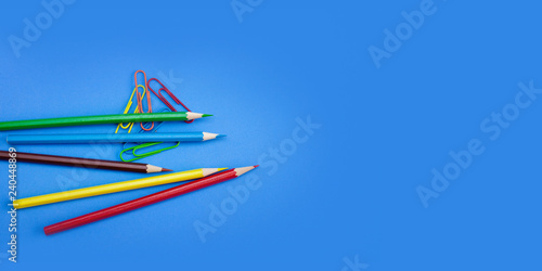 Web banner, poster wide template design concepts of stationery supplies, Colored crayon pencils and clips on blue background with copy space. Top view, Closeup.