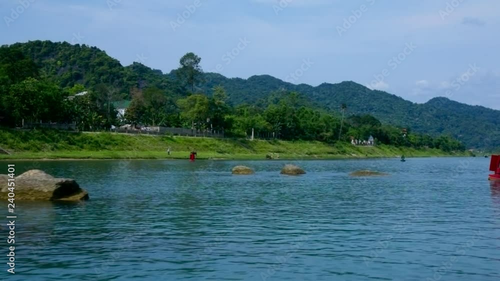 sailing past pictorial forestry bank of tropical river and buoys on rippling water under clear blue sky sailing past pictorial forestry bank of tropical river and buoys on rippling water under clear blue sky