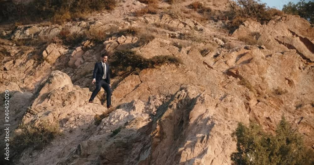 Young businessman in suit and tie making little steps, trekking in mountains, representing way to success - 4k Young businessman in suit and tie making little steps, trekking in mountains, representing way to success - 4k