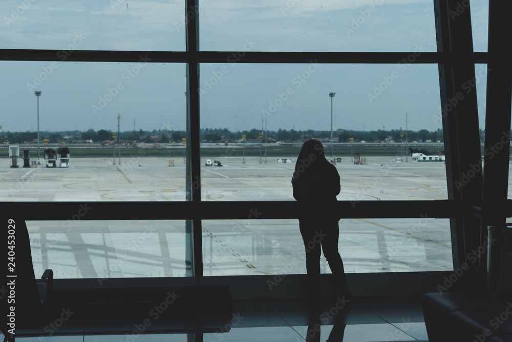 Fototapeta premium view of airport tarmac from within airport with person looking out of window