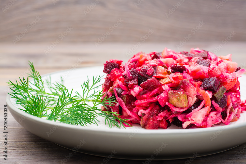 A portion of vinaigrette - a salad of boiled vegetables, sauerkraut and pickled cucumbers on a plate on a wooden table. National Russian dish A portion of vinaigrette - a salad of boiled vegetables, sauerkraut and pickled cucumbers on a plate on a wooden table. National Russian dish