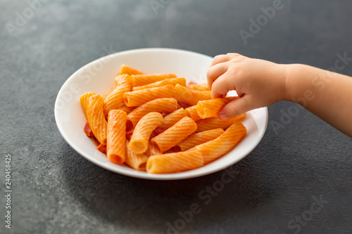 Little child eats fresh penne pasta with tomato sauce