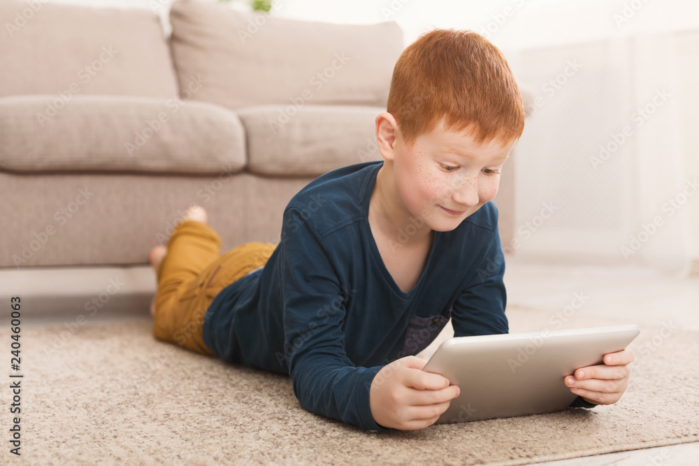 Redheaded boy playing on digital tablet on carpet Redheaded boy playing on digital tablet on carpet