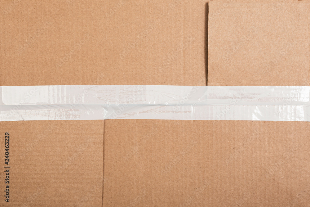 Corrugated cardboard with a white sticky tape. Cardboard box background.  Photos | Adobe Stock