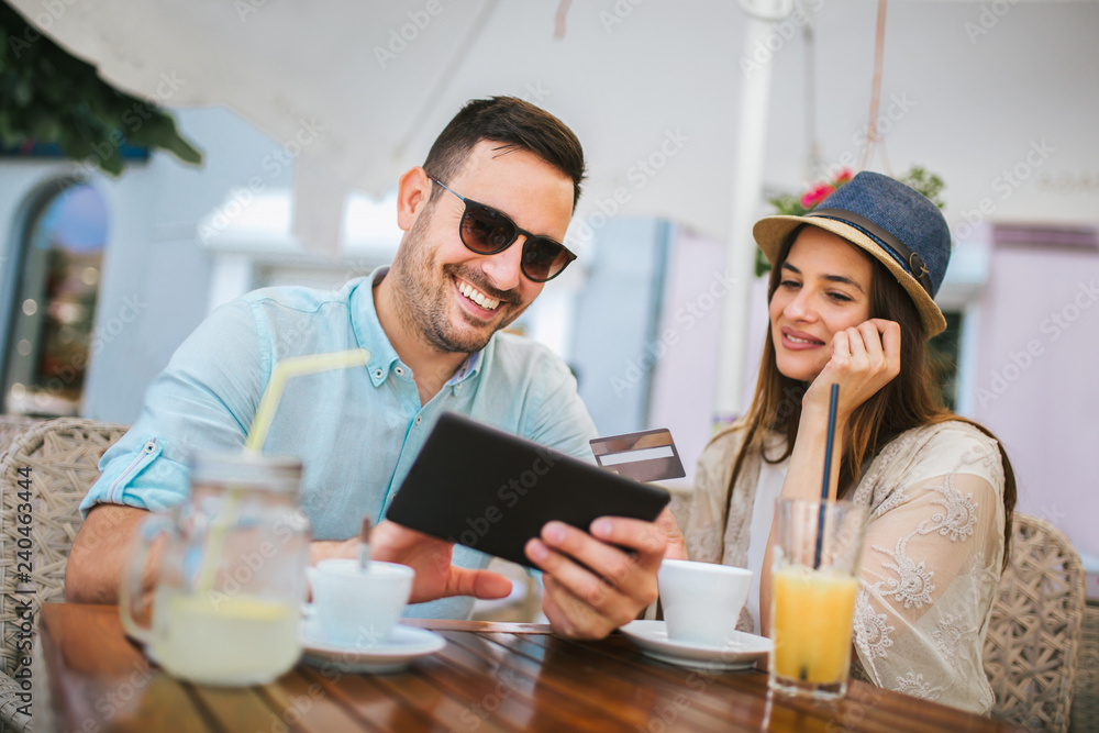Happy young couple shopping online while sitting in a cafe.