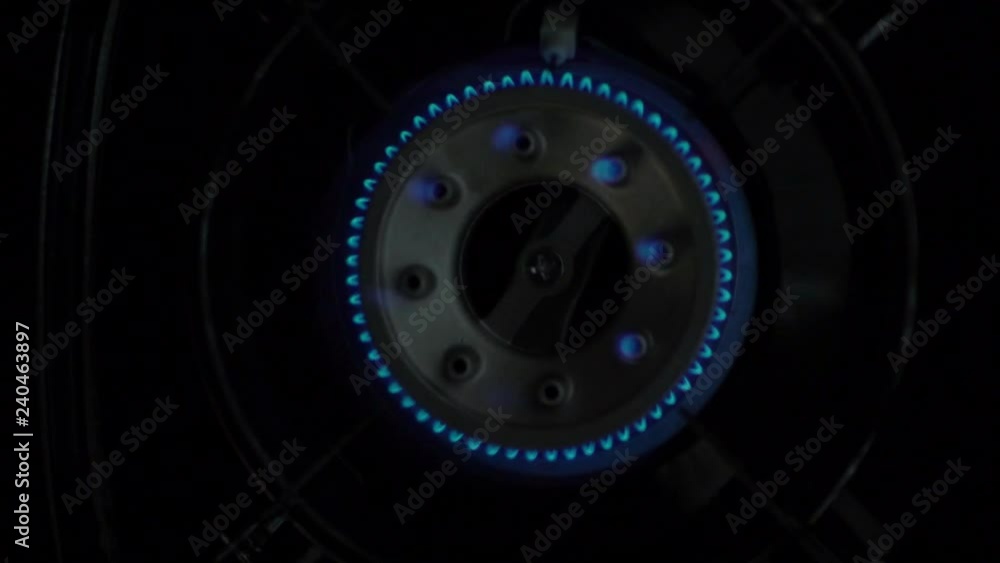 Closeup of kitchen stove with blue flame from burning gas on dark background Closeup of kitchen stove with blue flame from burning gas on dark background