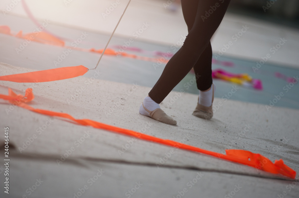 Spirals with orange art ribbon in fitness class. Young little gymnast girl in black sportswear dress, doing rhythmic gymnastics exercise with orange ribbon