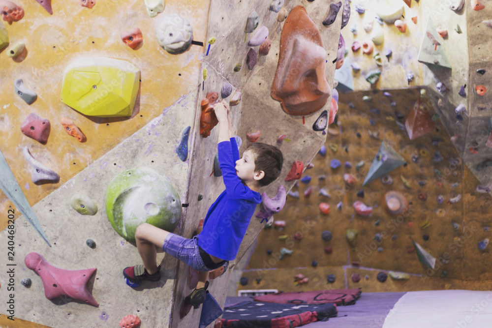 Fototapeta premium Little boy climbing a rock wall indoor.