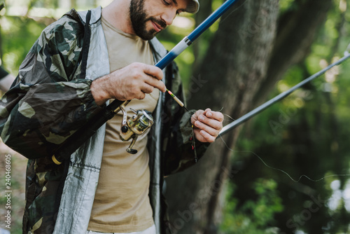 Pleasant bearded man fixing the hook of his rod