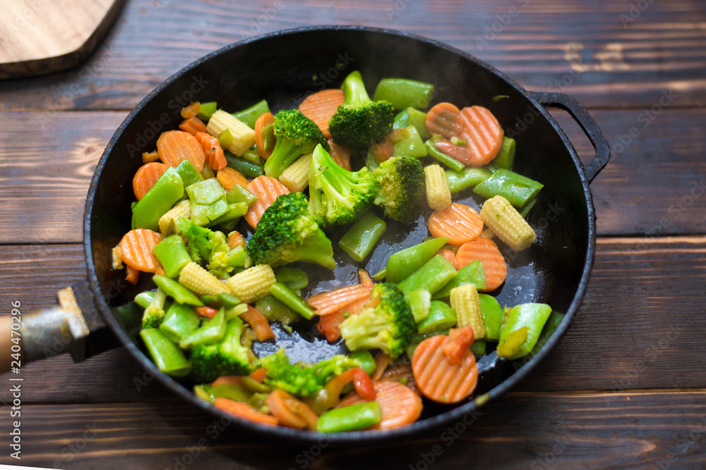 A mixture of frozen different vegetables in a pan on a wooden background. A mixture of frozen different vegetables in a pan on a wooden background.