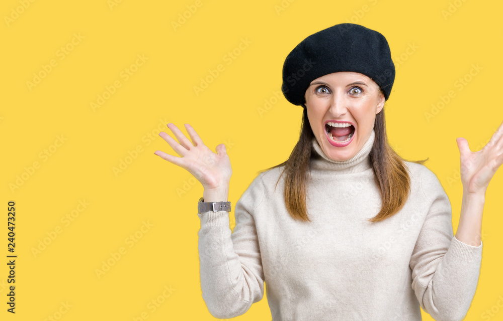 Middle age mature woman wearing winter sweater and beret over isolated background celebrating crazy and amazed for success with arms raised and open eyes screaming excited. Winner concept Middle age mature woman wearing winter sweater and beret over isolated background celebrating crazy and amazed for success with arms raised and open eyes screaming excited. Winner concept