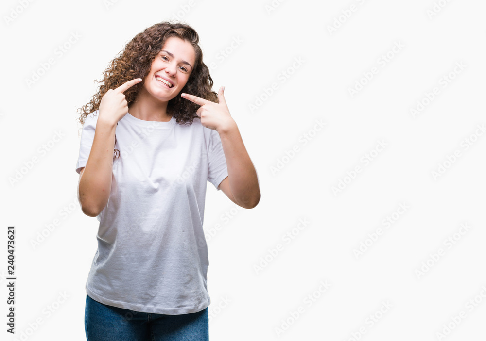 Beautiful brunette curly hair young girl wearing casual t-shirt over isolated background smiling confident showing and pointing with fingers teeth and mouth. Health concept. Beautiful brunette curly hair young girl wearing casual t-shirt over isolated background smiling confident showing and pointing with fingers teeth and mouth. Health concept.
