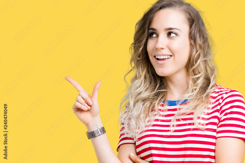 Beautiful young blonde woman over isolated background with a big smile on face, pointing with hand and finger to the side looking at the camera. Beautiful young blonde woman over isolated background with a big smile on face, pointing with hand and finger to the side looking at the camera.