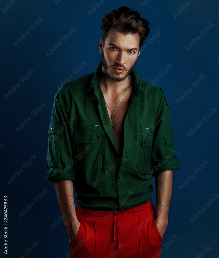 Fashion portrait of young man in green shirt and red pants poses over dark  blue wall with contrast light Stock Photo | Adobe Stock