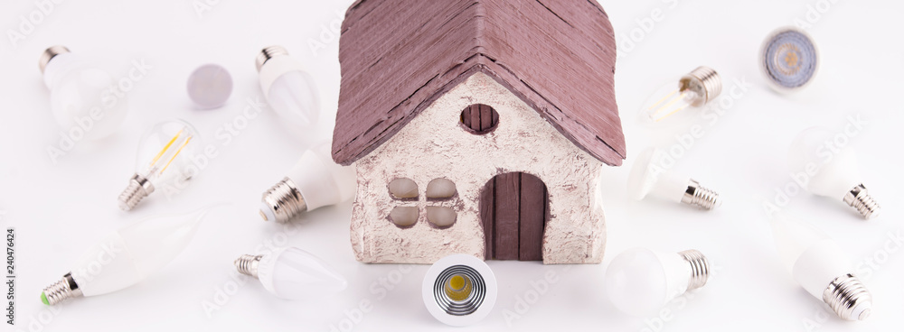 Led lamps lie near the house layout on a white background. Theme energy saving in the house Led lamps lie near the house layout on a white background. Theme energy saving in the house