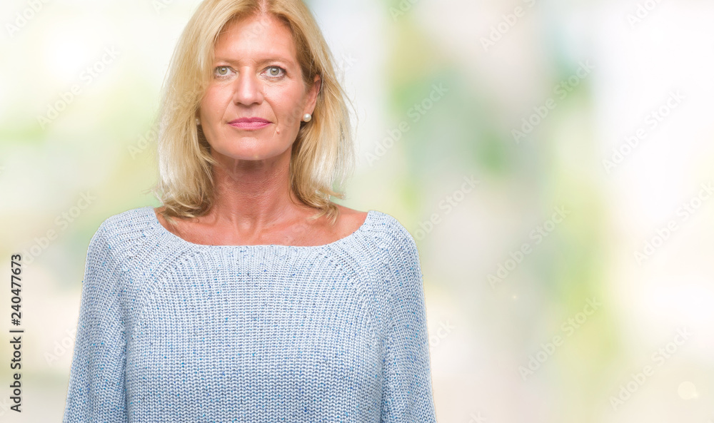Middle age blonde woman wearing winter sweater over isolated background with serious expression on face. Simple and natural looking at the camera. Middle age blonde woman wearing winter sweater over isolated background with serious expression on face. Simple and natural looking at the camera.