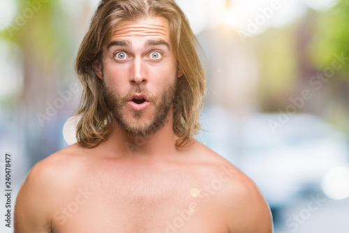 Young handsome shirtless man with long hair showing sexy body over isolated background afraid and shocked with surprise expression, fear and excited face.