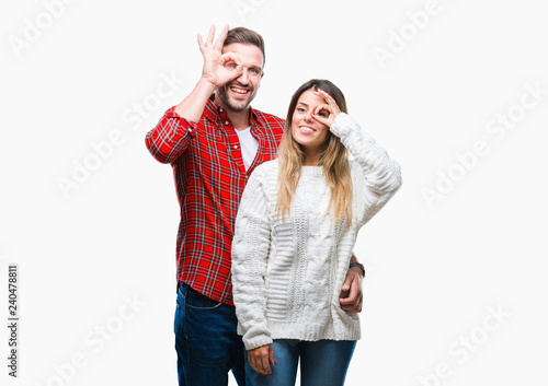 Young couple in love wearing winter sweater over isolated background doing ok gesture with hand smiling, eye looking through fingers with happy face.